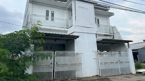 A two-story building with a white exterior, a balcony on the upper floor, and a gated entrance. - Hotel O Kost Aisyah Near Citra Grand Galesong City(Pattalassang) (Pattallassang)