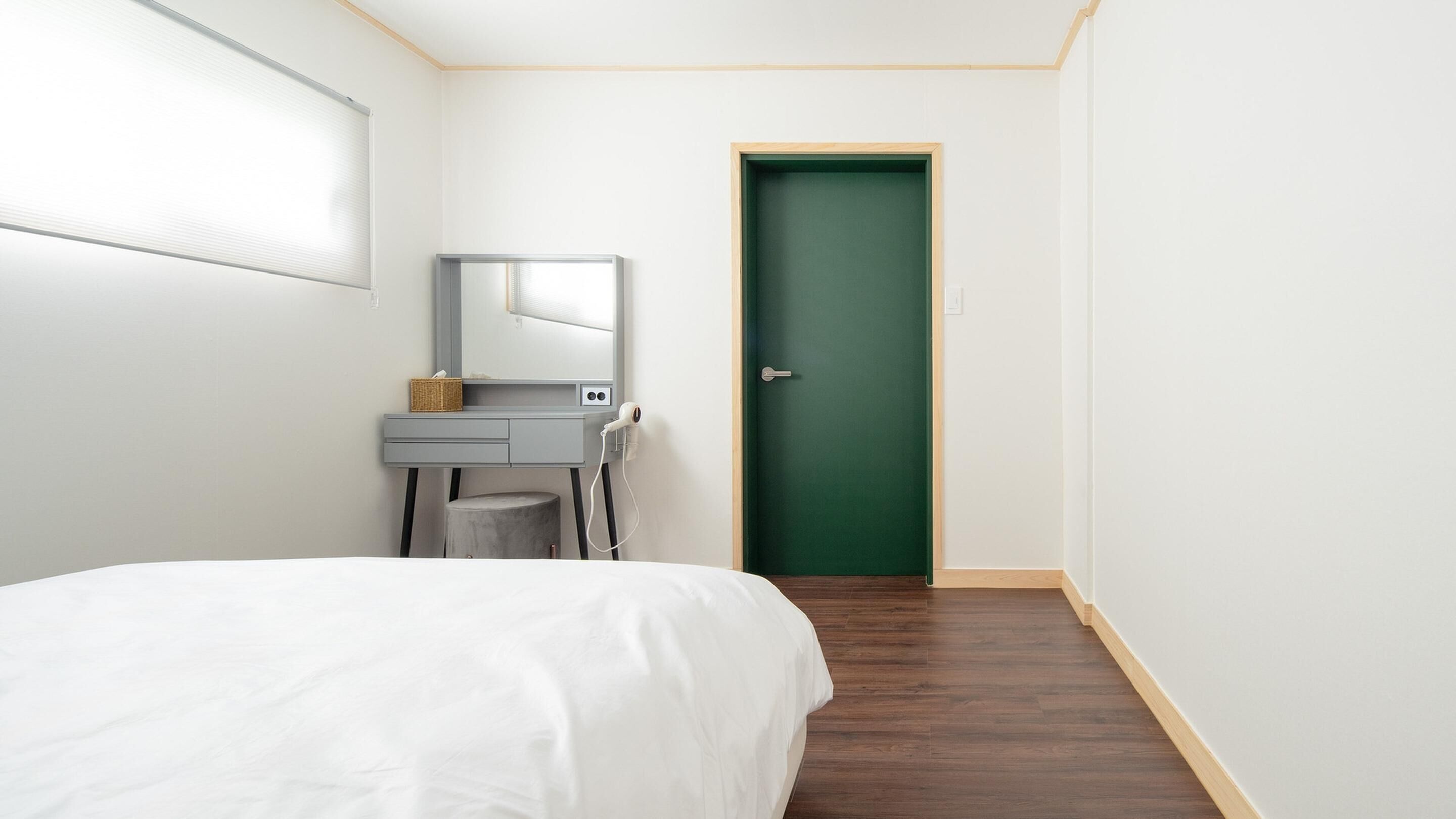 A bedroom with a bed, a desk with a mirror, a hairdryer, and a green door.