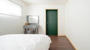 A bedroom with a bed, a desk with a mirror, a hairdryer, and a green door.