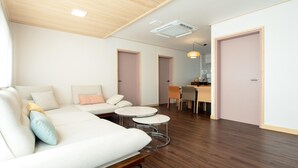 A modern living room with a sofa, two round tables, and a dining area with chairs. - Jeju Staysosoheon Dokchae Pension (Jeju City)