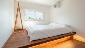 A bedroom with a bed, wooden floor, a ladder, a window with a view, and a wall-mounted light fixture. - Jeju Staysosoheon Dokchae Pension (Jeju City)
