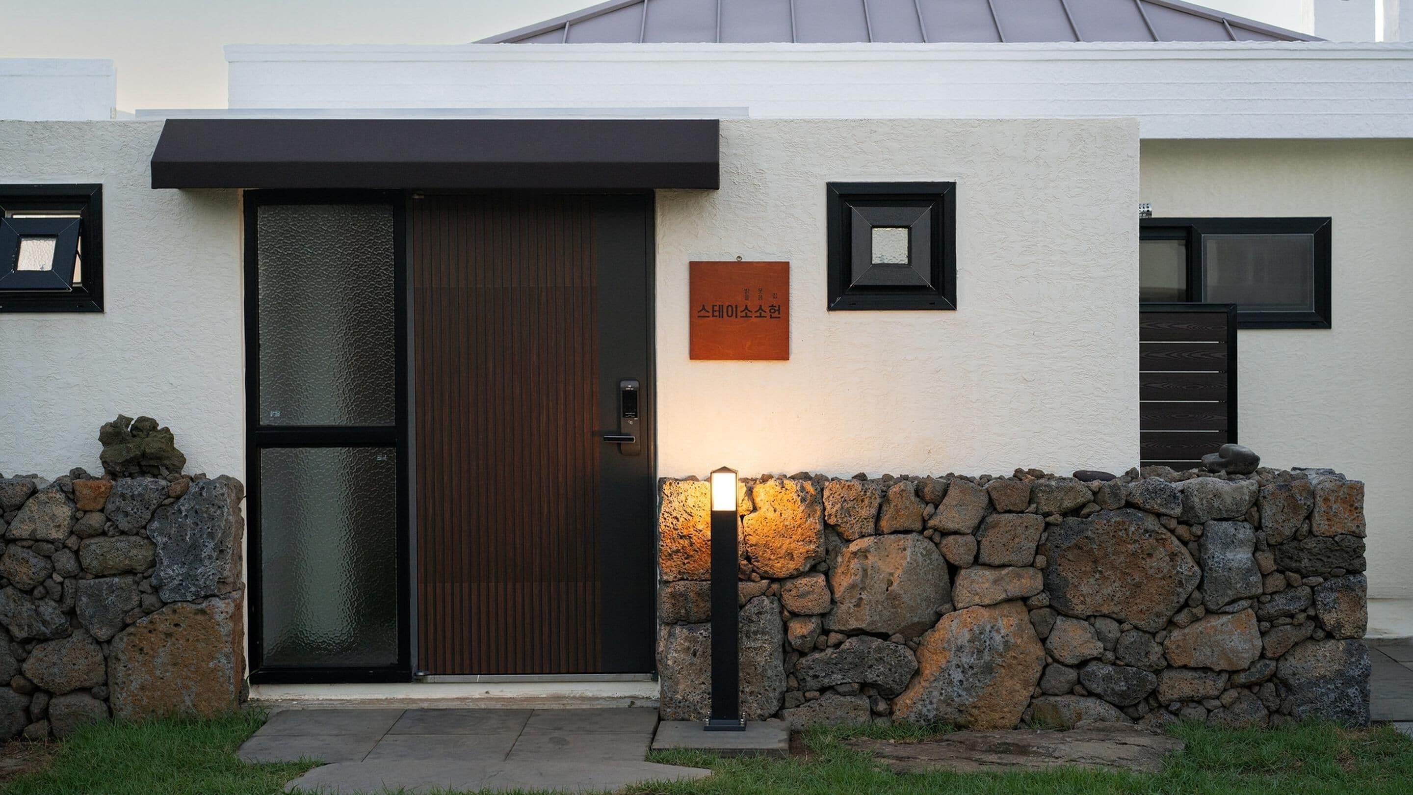 Un edificio moderno con un muro de piedra, una puerta de madera y un cartel con texto en coreano.