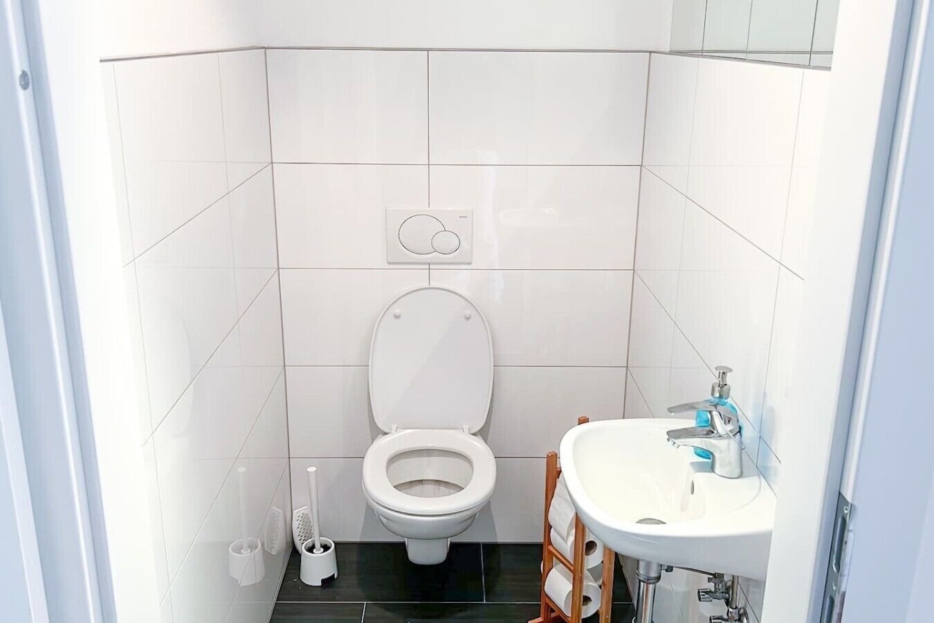 Une petite salle de bain moderne, équipée de toilettes, d’un lavabo et d’un porte-rouleau de papier toilette.