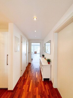 A hallway with wooden flooring, white walls, and a ceiling light.
