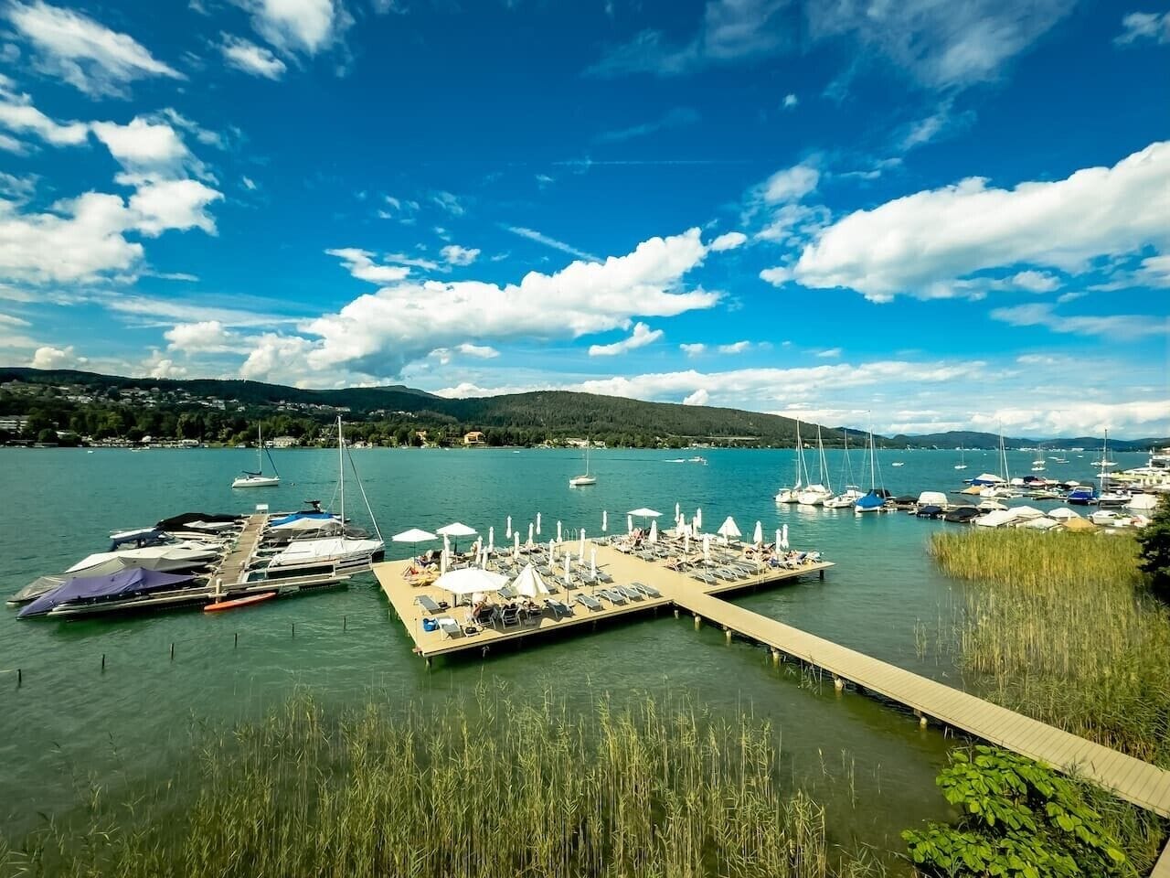 A marina with boats docked, a pier with sun loungers, and a clear blue sky.