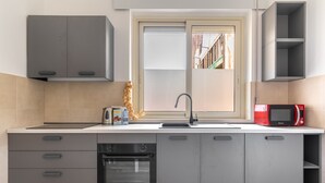 Cozinha moderna com armários cinza, forno embutido, micro-ondas e janela com vista para edifícios.