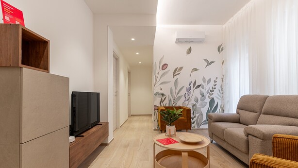 Uma sala de estar moderna com um sofá, uma televisão, um armário de madeira e uma pequena mesa com uma planta.
