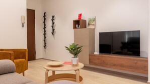 Uma sala de estar moderna com um sofá, uma mesa de madeira pequena, uma planta em vaso, uma televisão e um armário de madeira.
