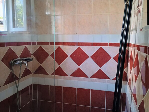 A bathroom with a shower area featuring a red and beige diamond-patterned tile design.
