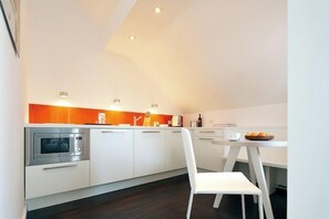 A modern kitchen with white cabinets, a built-in oven, and a dining area with a white chair and table. - ipartment Köln City (Cologne)