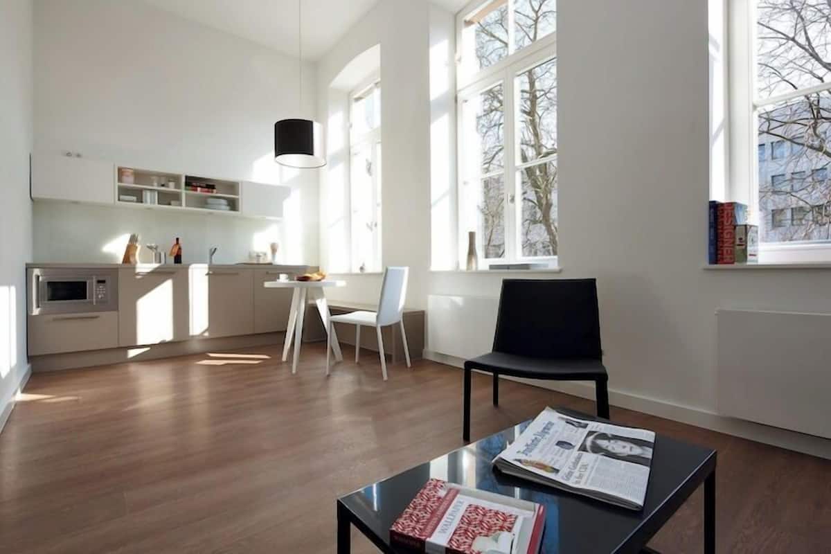 A modern kitchen with white cabinetry, a dining area with a black chair, and a window with a view of bare trees.