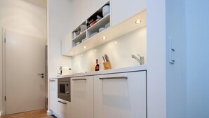 Ett modernt kök med vita skåp, en inbyggd ugn och en hylla med tallrikar och köksredskap.