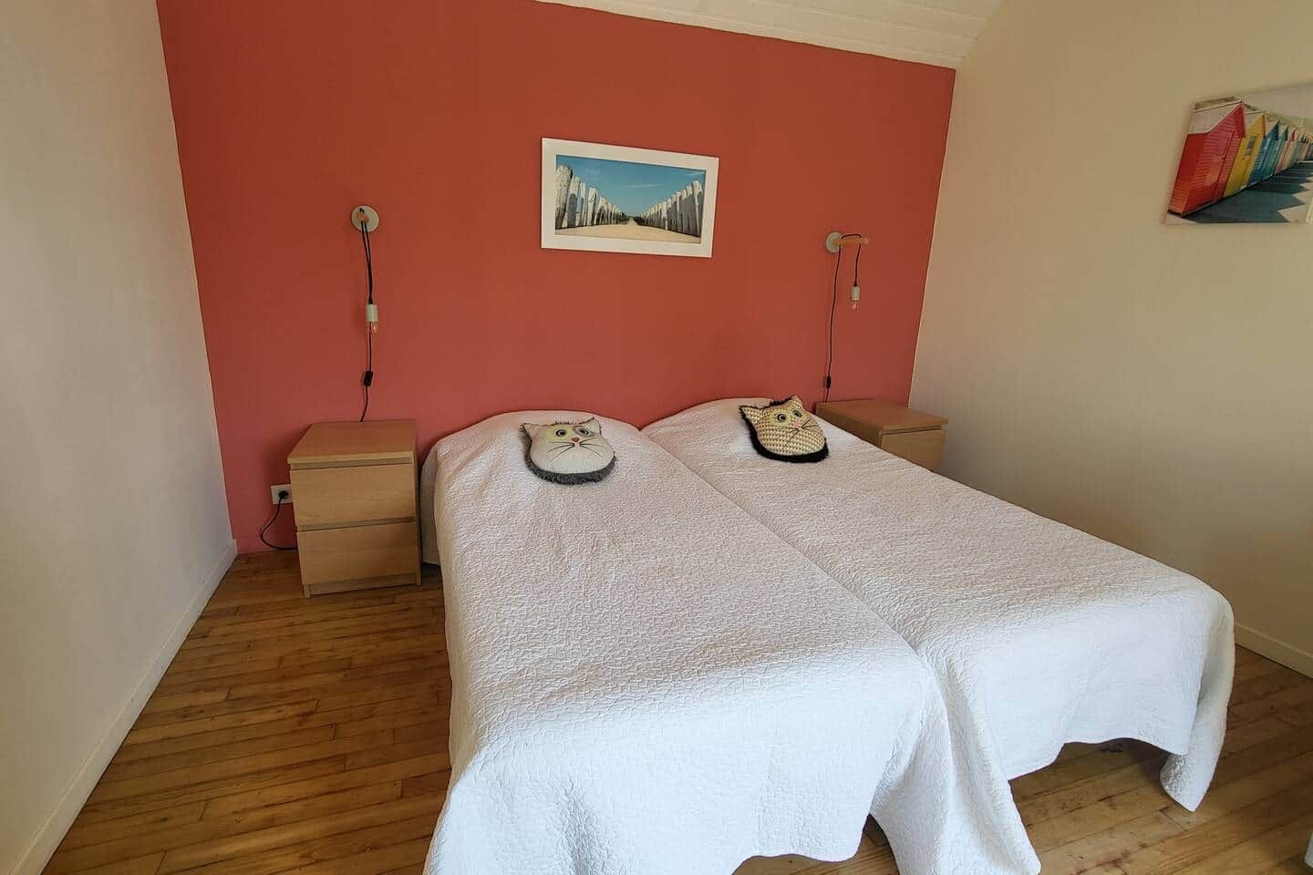 Une chambre avec deux lits, une commode en bois, un tableau au mur et une petite table avec une lampe.