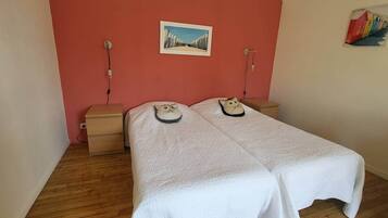 Une chambre avec deux lits, une commode en bois, un tableau au mur et une petite table avec une lampe.