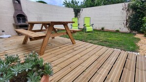 A wooden deck with a picnic table and chairs, a potted plant, and a brick oven in the background.