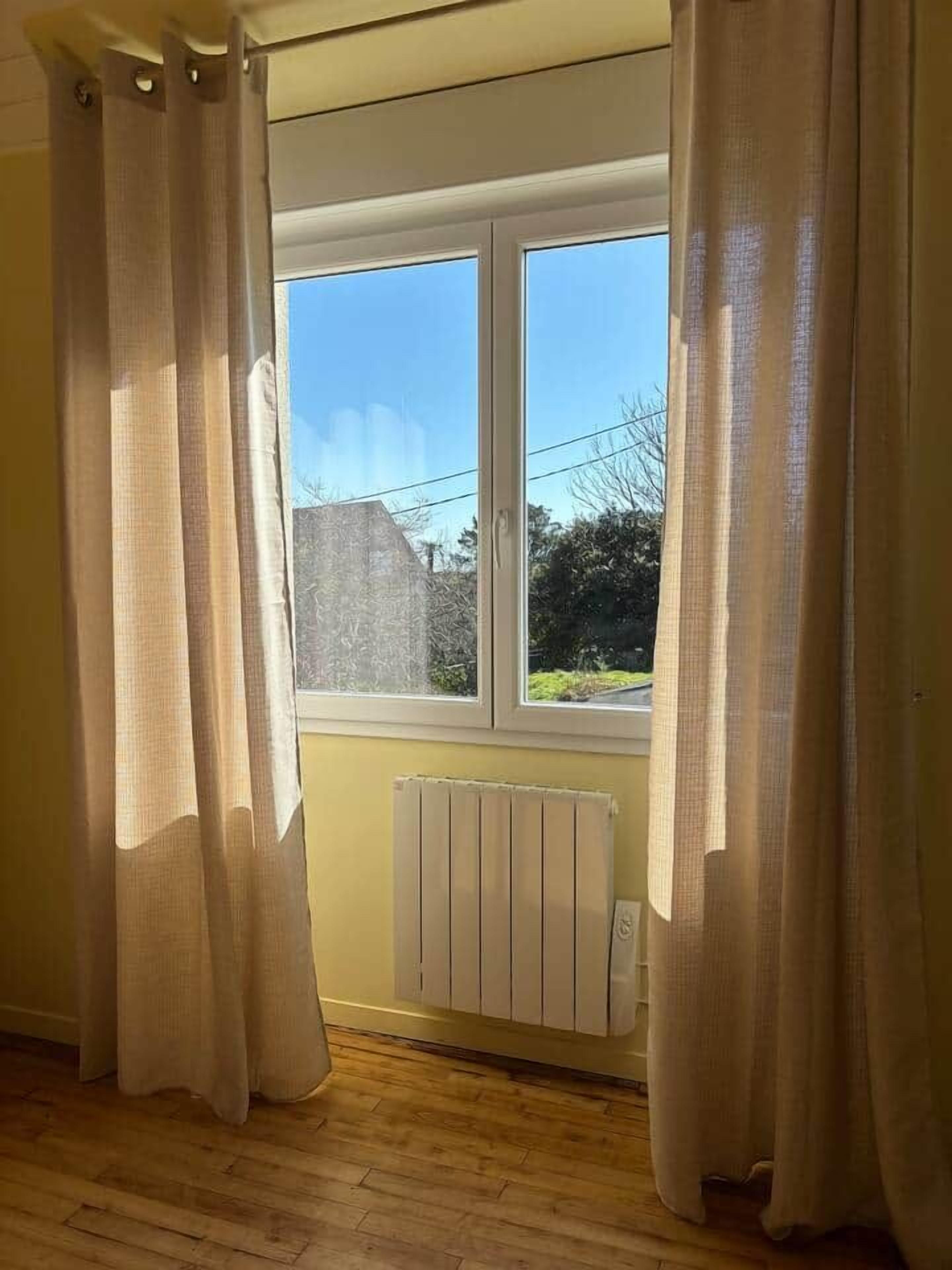 Une pièce avec une fenêtre, des rideaux, un radiateur et un plancher en bois.
