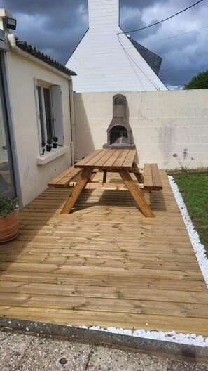 En udendørs træterrasse med grill og bord.