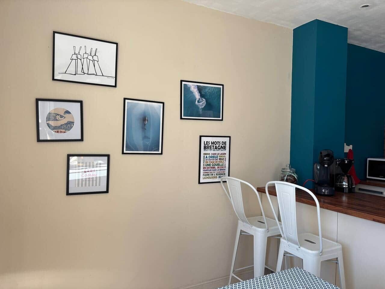 Une pièce avec un mur de couleur beige, un mur d’accent bleu et une chaise blanche. Des œuvres d’art encadrées ornent le mur, et une machine à café est posée sur le comptoir.