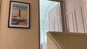 A hallway with wooden paneling, a framed picture of a lighthouse, and a staircase leading to another room.