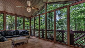Un espacio al aire libre techado con una terraza de madera, un sofá con cojines y una mesa de centro.