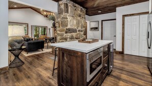 Un amplio salón con una pared de acento de piedra, una cocina con electrodomésticos de acero inoxidable y un techo de madera.