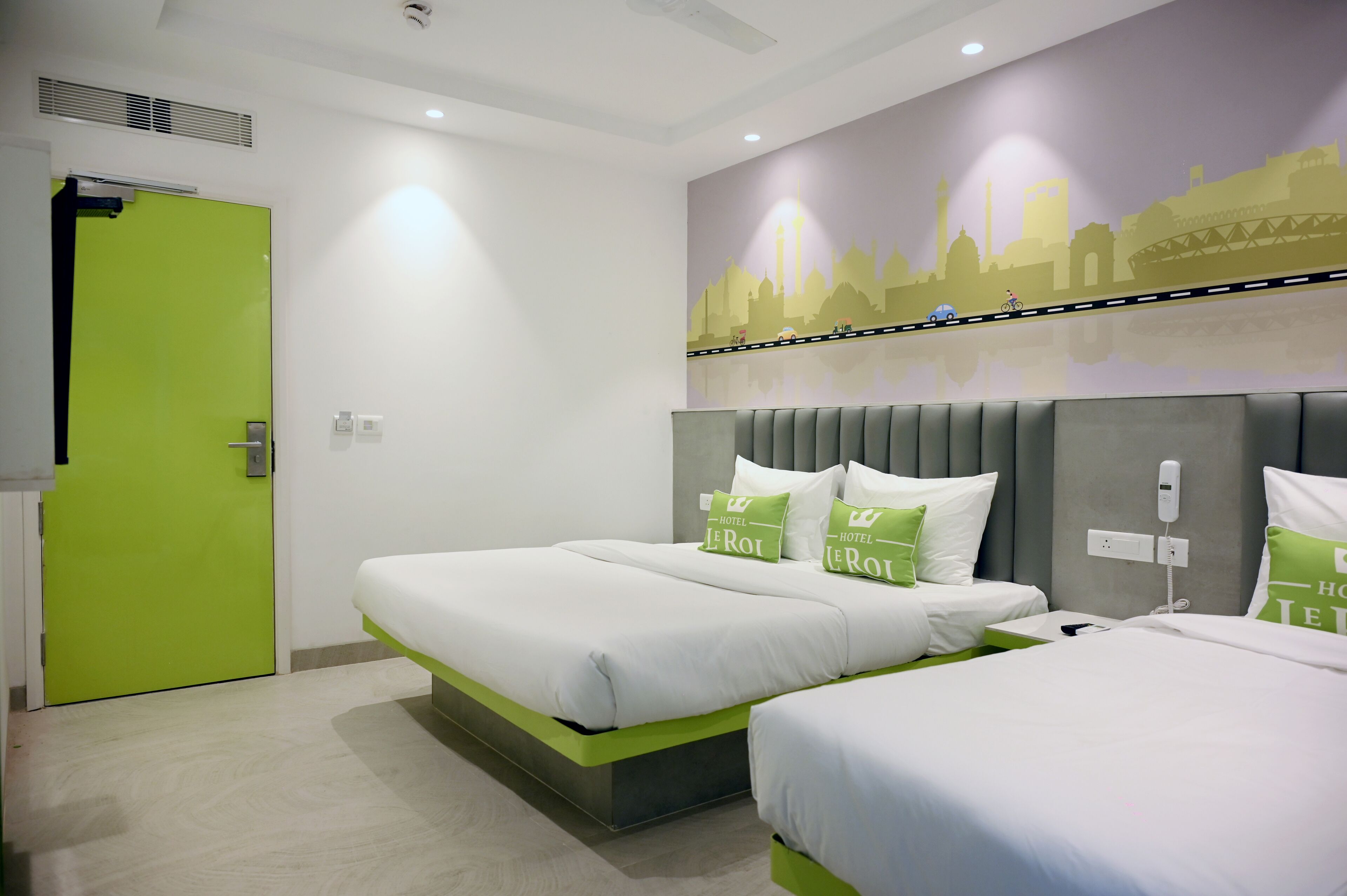 A hotel room with two beds, a green door, and a cityscape mural on the wall.