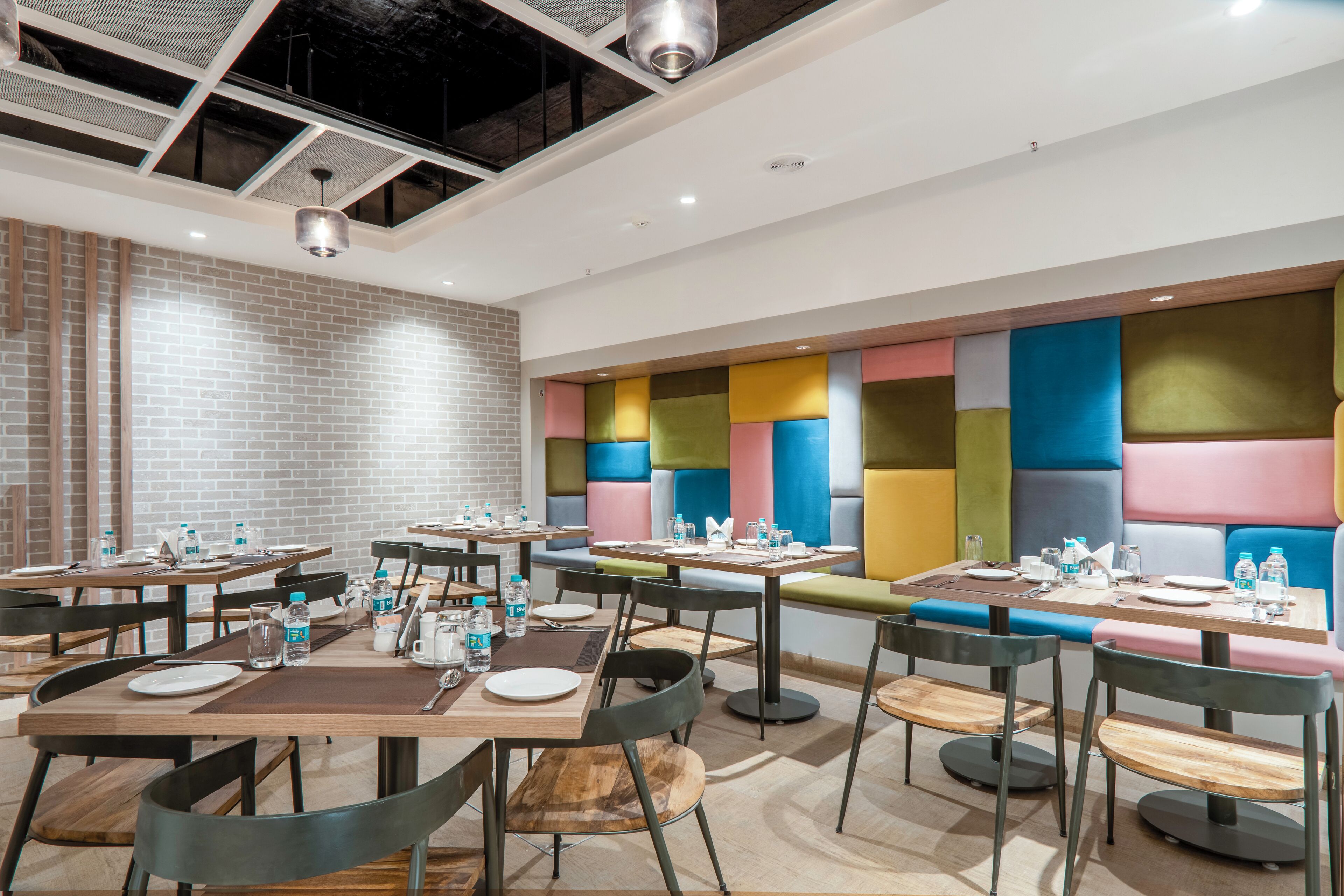 A modern dining area with multiple tables and chairs, equipped with water bottles and cutlery.