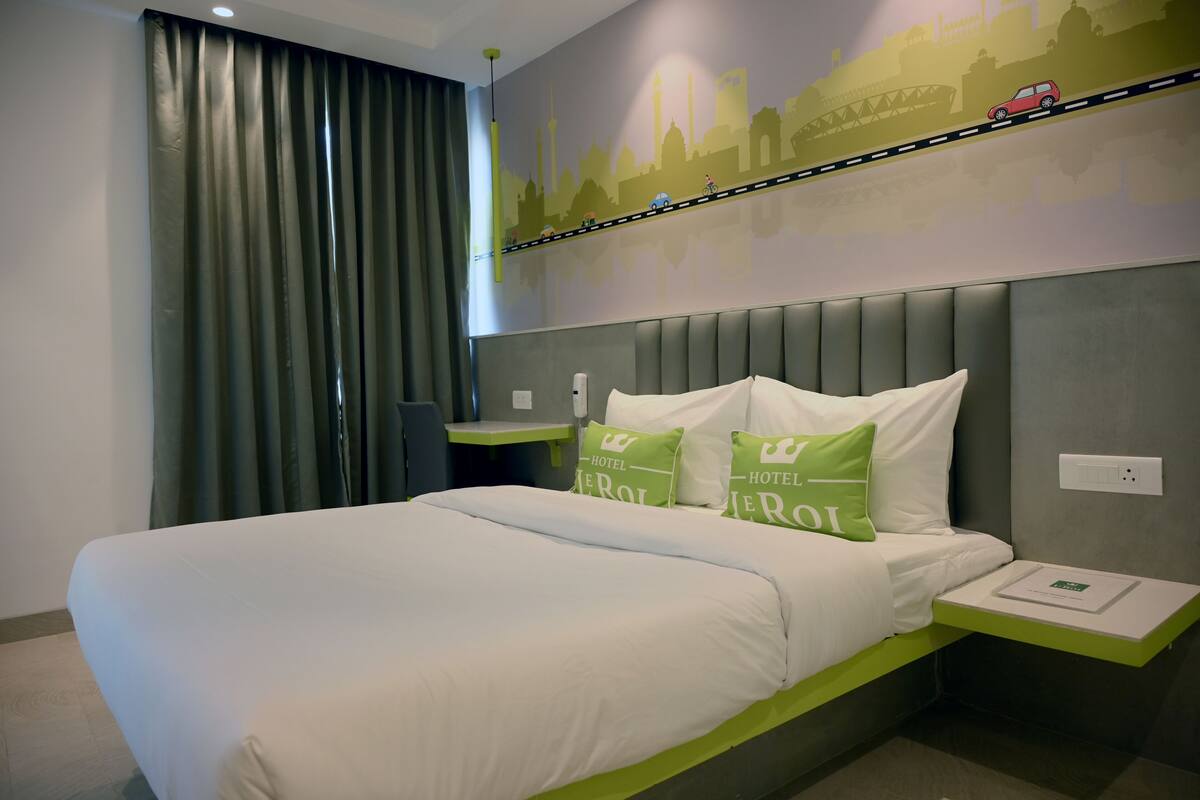 A hotel room with a bed, a nightstand, a wall with a cityscape mural, and a window with curtains.
