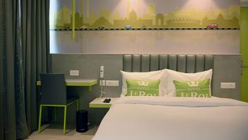 A hotel room with a bed, a desk, a chair, a nightstand, and a wall mural.