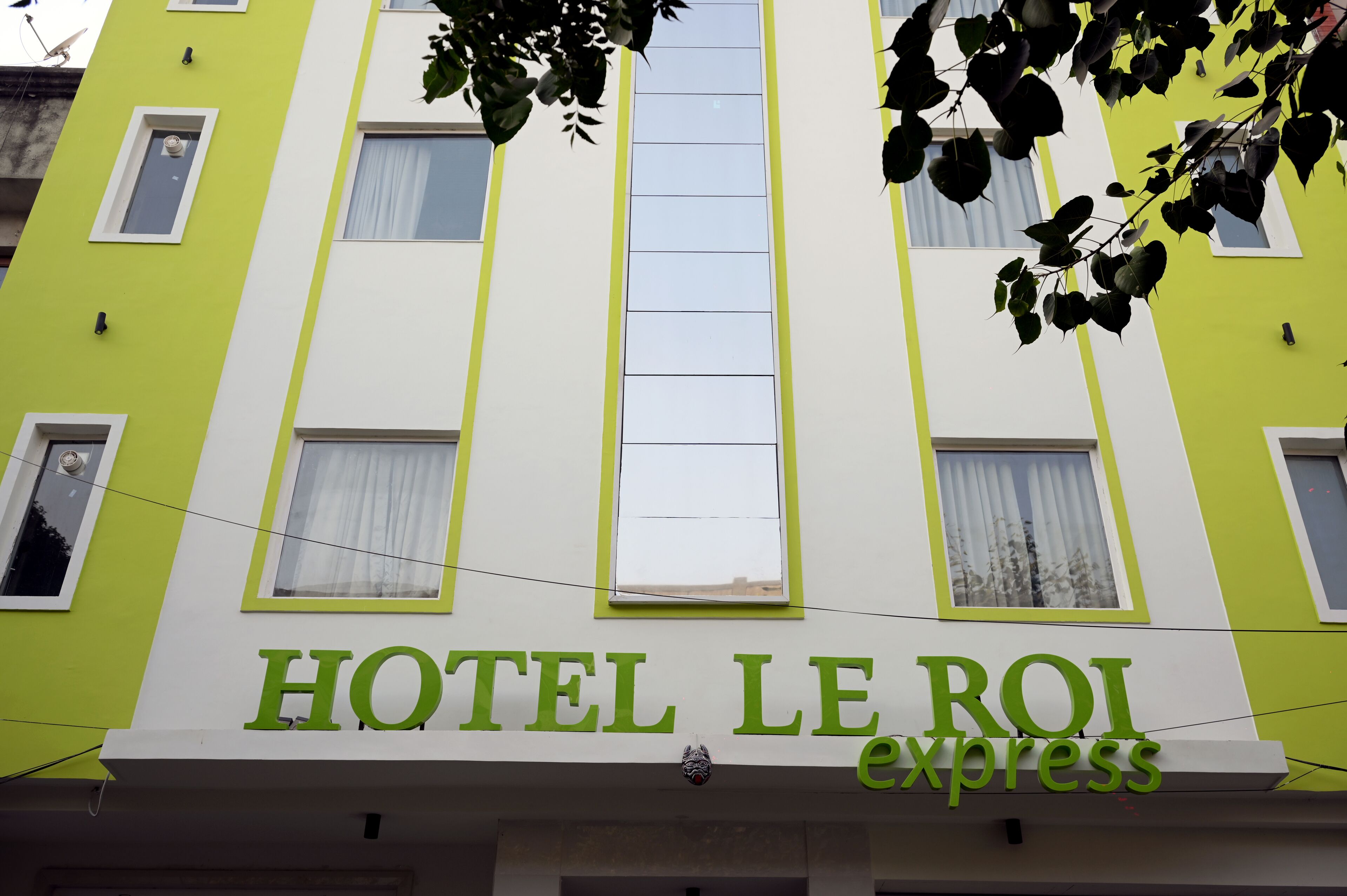 A hotel named HOTEL LE ROI express with a green and white facade, multiple windows, and a visible door.