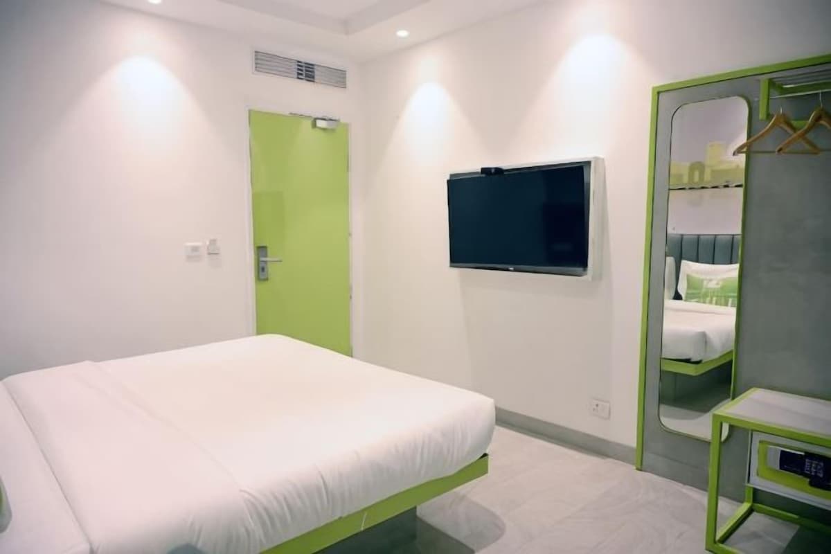 Una habitación de hotel moderna con una cama, un televisor, un espejo y una puerta verde.