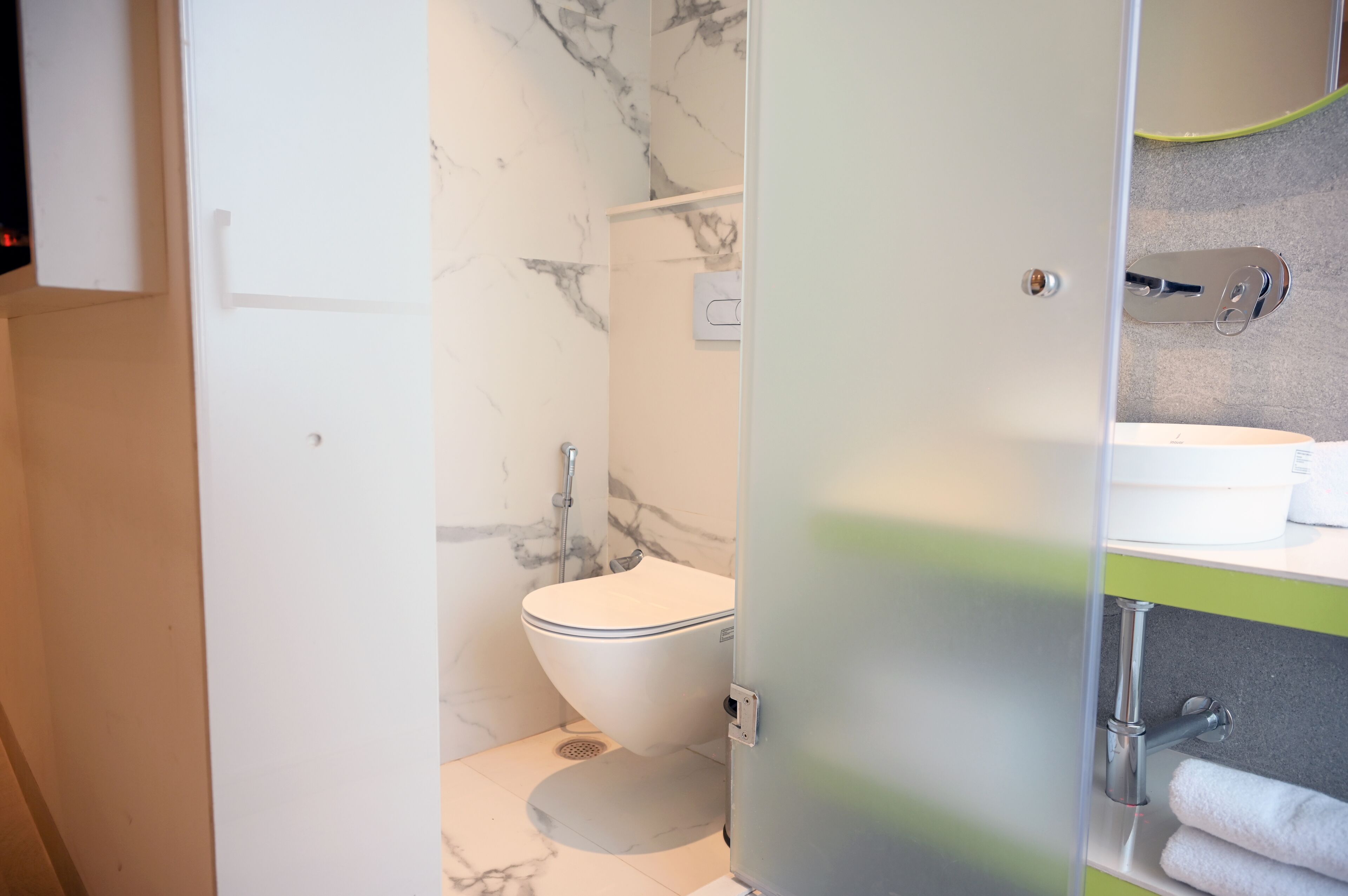 A modern bathroom with a marble wall, a toilet, and a sink with a towel rack.