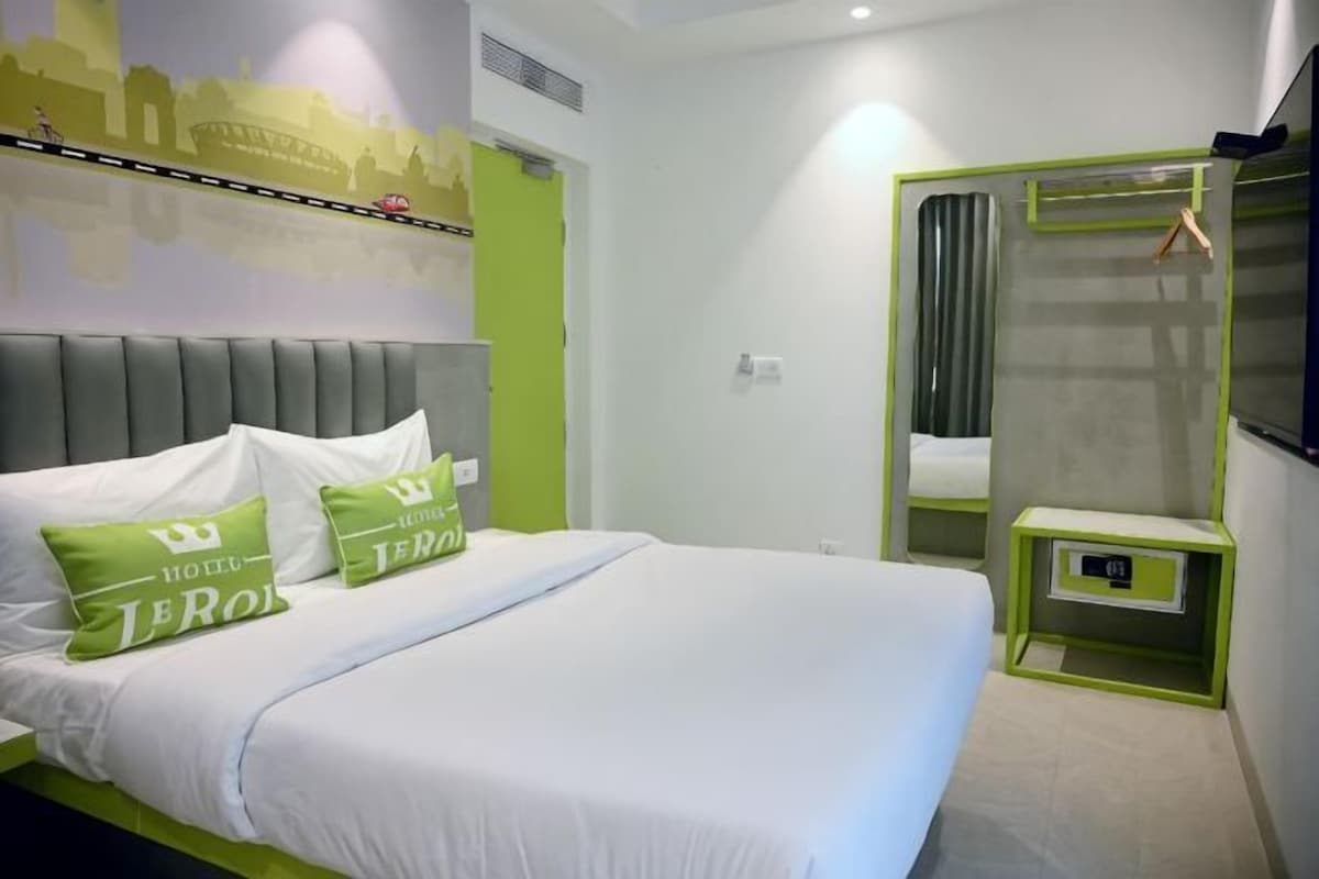 Una habitación de hotel con cama, almohadas, mesita de noche, espejo y ventana.