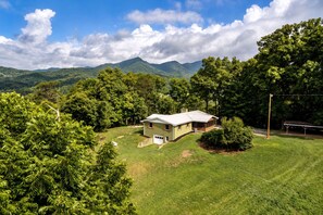 A single-story house with a sloped roof, surrounded by lush greenery and mountains in the background.