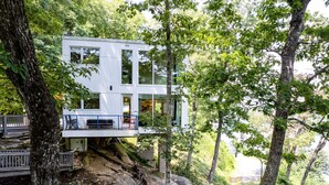 A modern house with a balcony, surrounded by trees and rocky terrain.