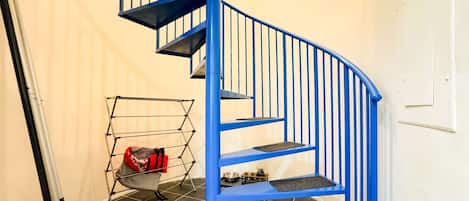 A blue spiral staircase in a room with tiled flooring and a metal drying rack with a red bag.