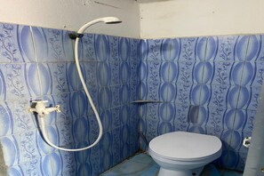 Un baño con azulejos florales azules, un inodoro blanco y una ducha con manguera.