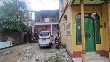 Un SUV blanco aparcado en una calle estrecha con una motocicleta a su lado, conduciendo hacia un edificio con una puerta verde y un balcón.