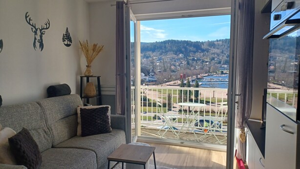 Ein Wohnzimmer mit einer Couch, einem kleinen Tisch und Blick auf eine Wohngegend mit Häusern und einem Gewässer.