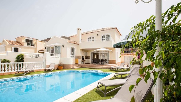 Ein Swimmingpool mit Liegestühlen, eine Terrassenfläche und ein großes Haus mit mehreren Balkonen.