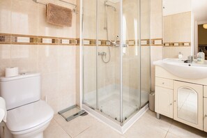 A bathroom with a glass-enclosed shower, a toilet, and a sink with a mirror.