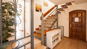 Eine Treppe mit Holzboden und Metallgeländern, ein weißer Konsolentisch mit Büchern, eine Holztür und ein Blumentopf.