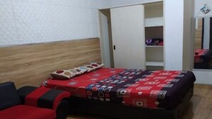 Una habitación con cama, armario y una pequeña mesa con colcha de cama estampada en rojo y negro.