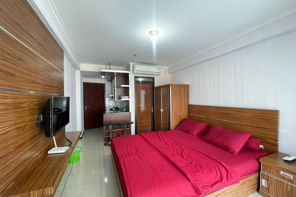 Une chambre d’hôtel avec un lit en bois, un bureau avec un ordinateur, une armoire et une salle de bain visible à travers une porte ouverte.