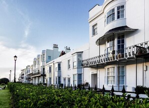 A row of white buildings with balconies, a clear sky, and a well-maintained hedge in the foreground. - Beautiful 5 Bedroom Regency House / Pets Welcome (Bognor Regis)