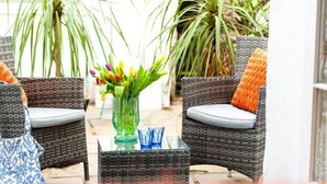 Une chaise en osier avec un coussin, une table en verre avec un vase de fleurs, et une autre chaise en osier avec un coussin.