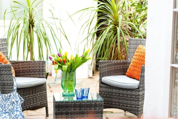 A wicker chair with a cushion, a glass table with a vase of flowers, and a wicker chair with a cushion.