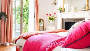 Une chambre à coucher avec un lit, une cheminée, un miroir et une fenêtre avec des rideaux.