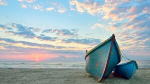 Deux bateaux sur une plage, avec un coucher de soleil en arrière-plan.