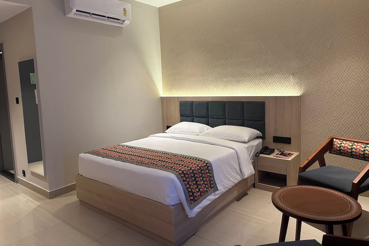 Ein modernes Hotelzimmer mit einem großen Bett, einem Nachttisch, einem Sessel und einer Klimaanlage.